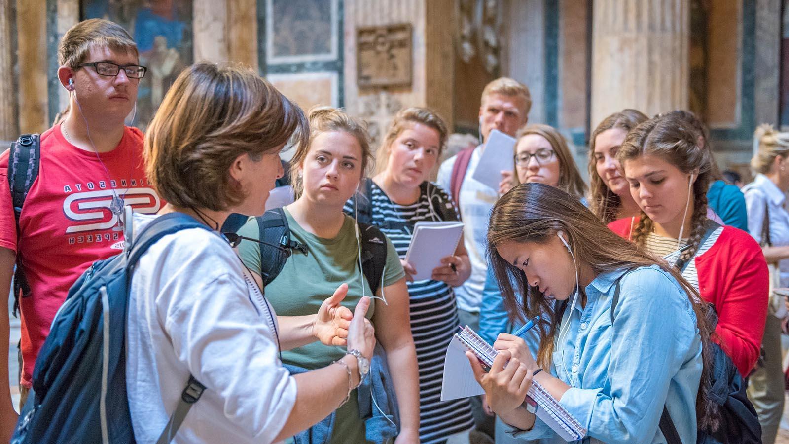 Study abroad students in the Pantheon in Rome, Italy, taking notes while listening to lecture by a professor