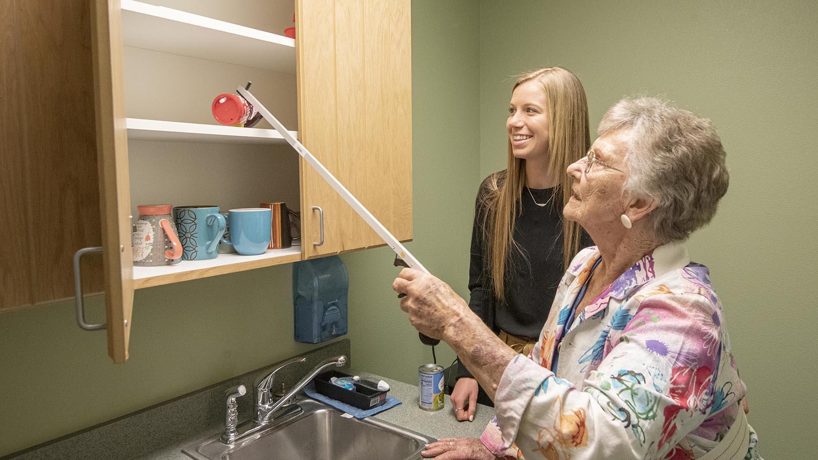 Occupational therapy doctoral student teaching an elderly client how to grab items from the cupboard
