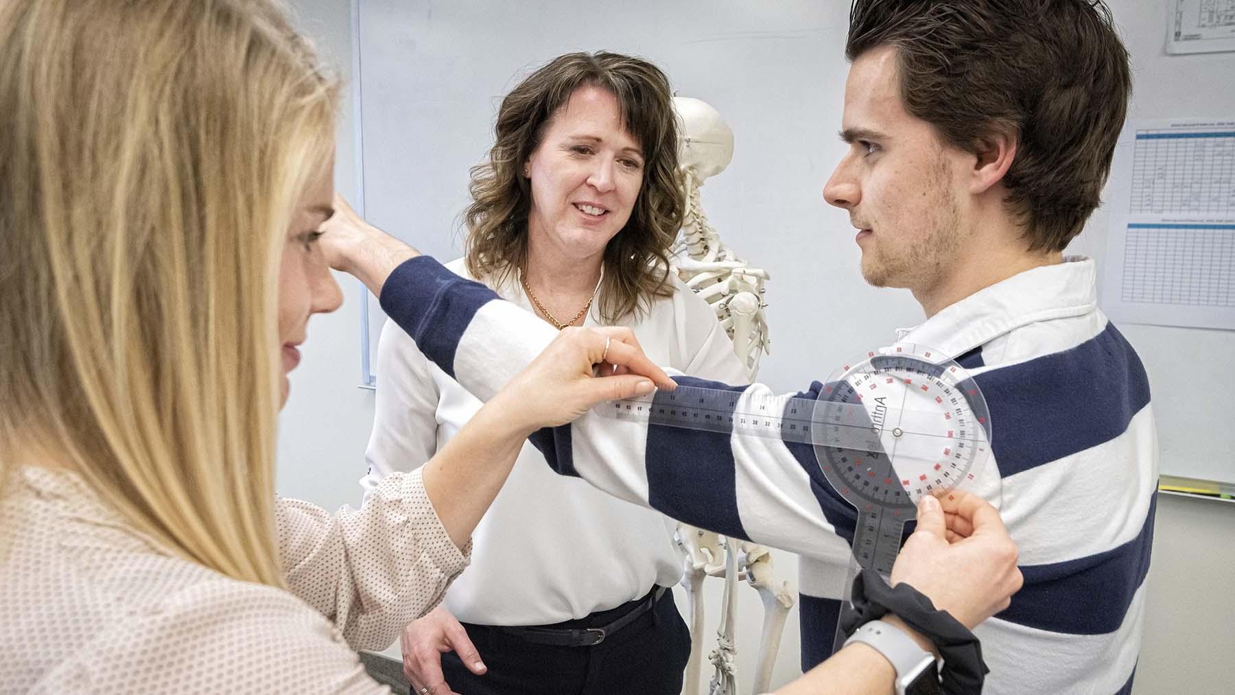 Occupational therapy student assessing shoulder movement of a classmate with the professor looking on